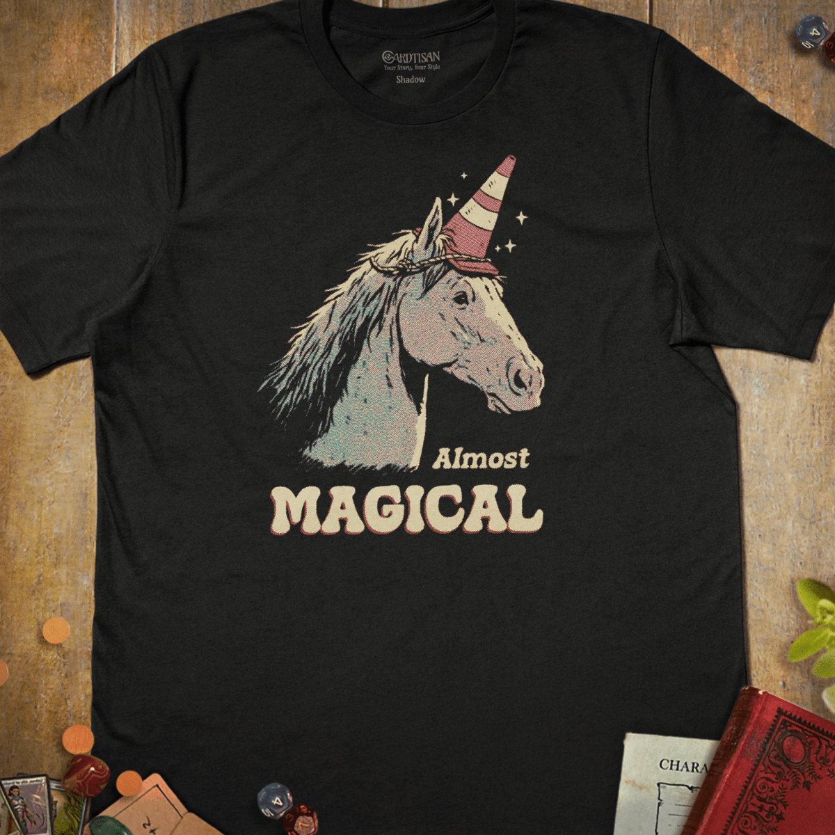 Black graphic T-shirt with a horse wearing a traffic cone as a unicorn horn illustration and "Almost Magical" text